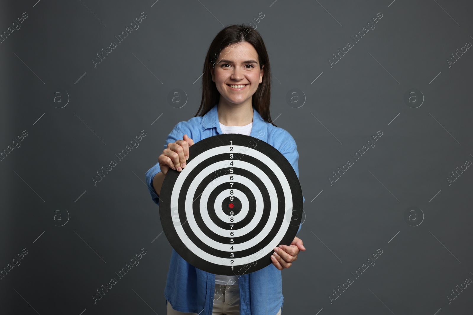 Targeting. Smiling woman with dart board on grey background Photo of Targeting. Smiling woman with dart board on grey background