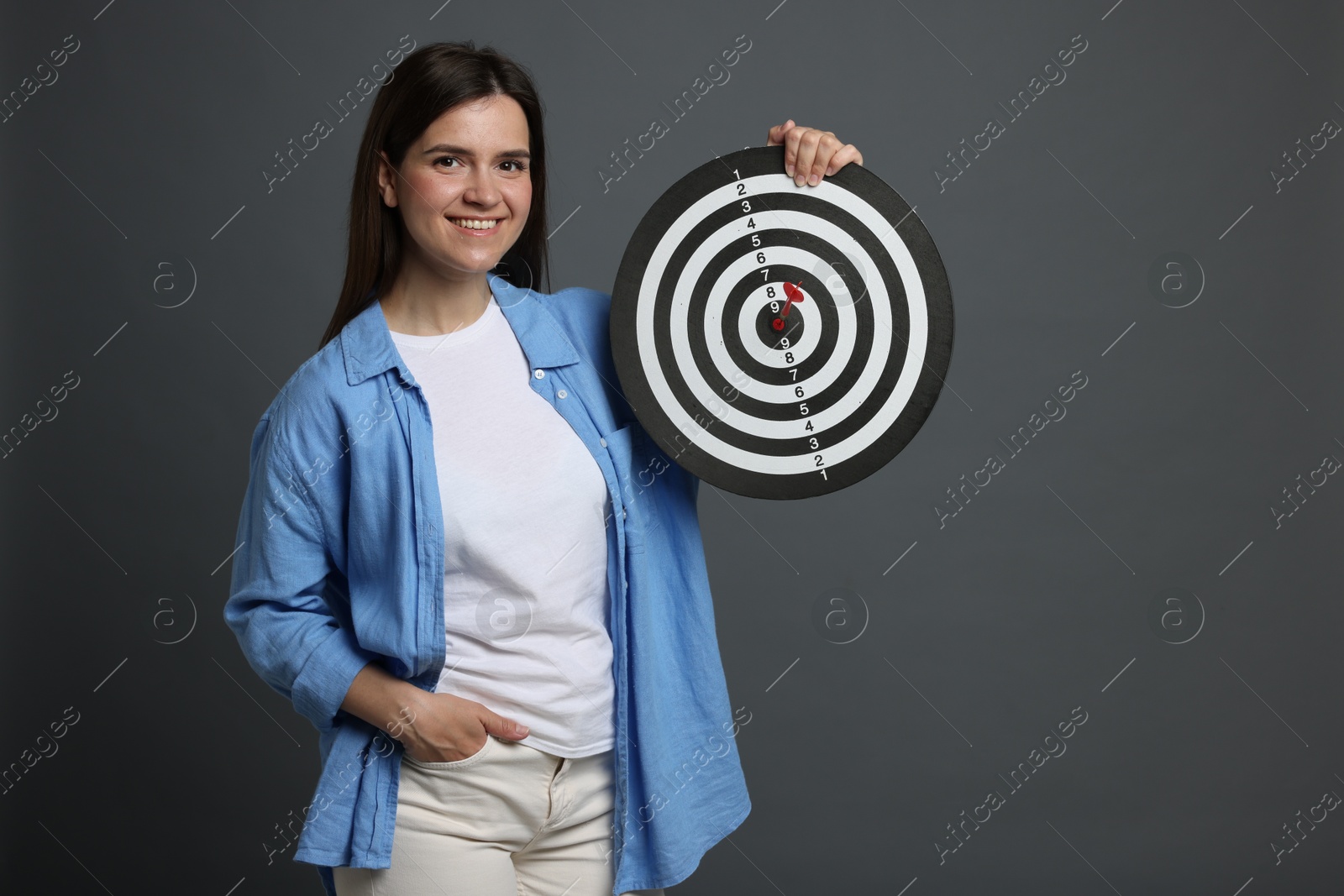 Targeting. Smiling woman with dart board on grey background Photo of Targeting. Smiling woman with dart board on grey background