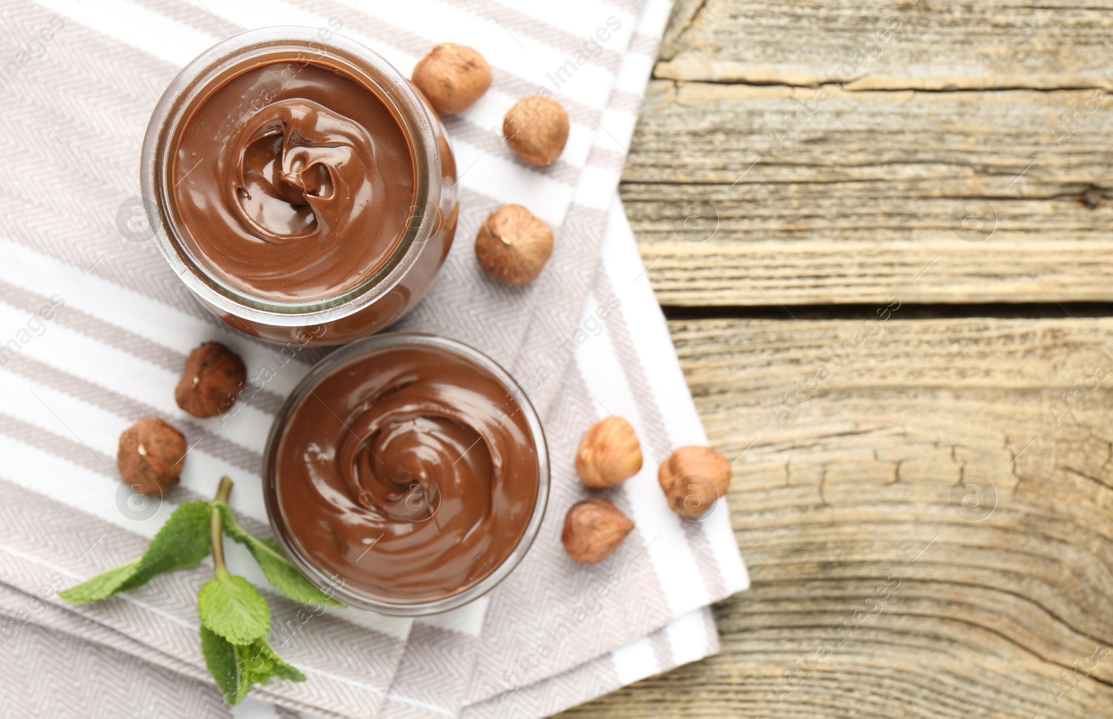 Photo of Tasty chocolate spread, hazelnuts and mint on wooden table, top view. Space for text