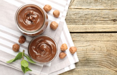 Photo of Tasty chocolate spread, hazelnuts and mint on wooden table, top view. Space for text