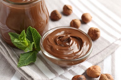 Photo of Tasty chocolate spread, hazelnuts and mint on striped tablecloth, closeup
