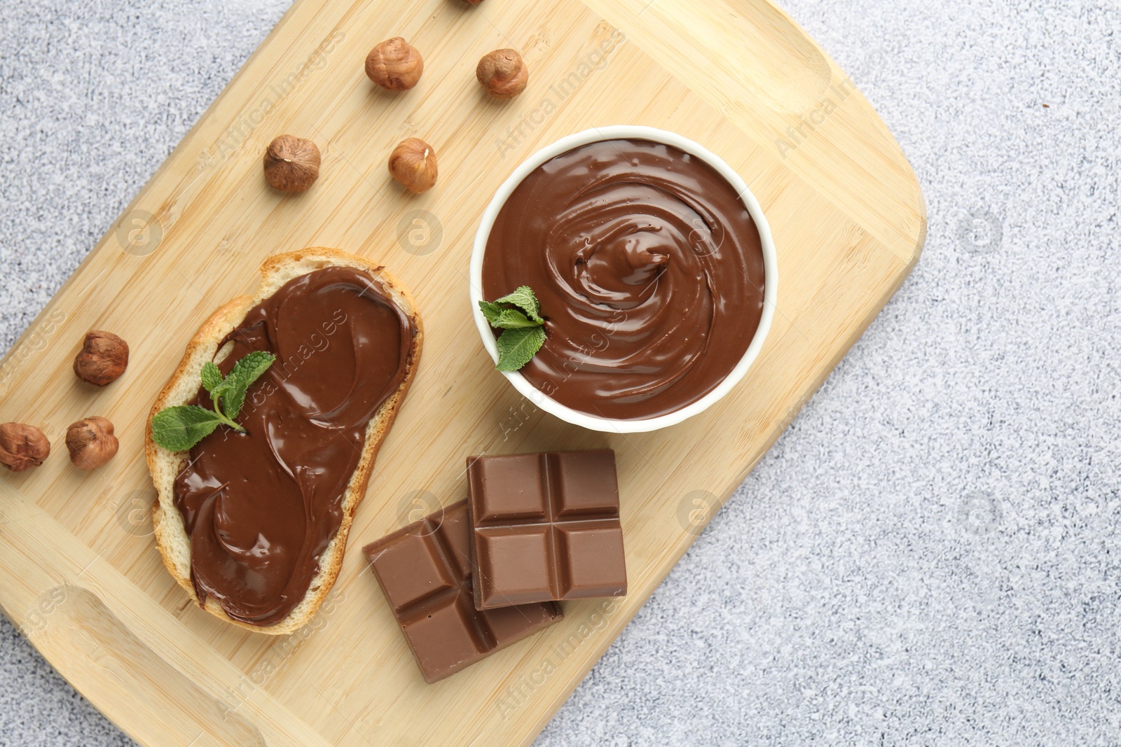 Tasty chocolate spread, toast, hazelnuts and mint on grey textured table, top view Photo of Tasty chocolate spread, toast, hazelnuts and mint on grey textured table, top view