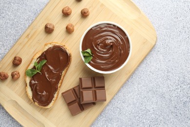 Photo of Tasty chocolate spread, toast, hazelnuts and mint on grey textured table, top view