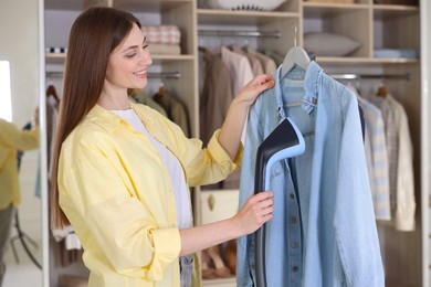 Photo of Smiling woman steaming shirt on hanger at home
