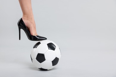 Photo of Woman in high heeled shoe with soccer ball on light background, closeup. Space for text