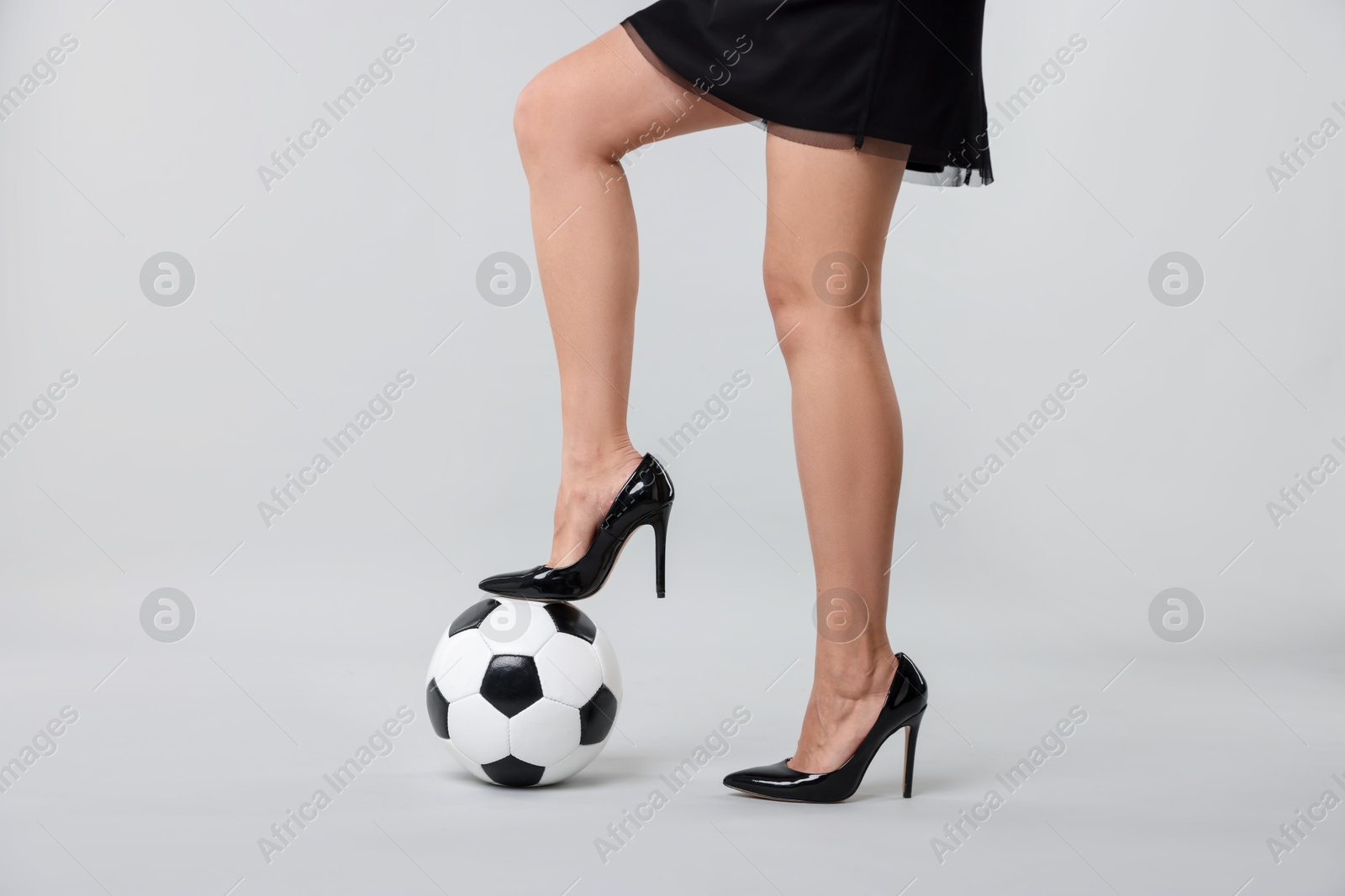 Photo of Woman in high heeled shoes with soccer ball on light background, closeup