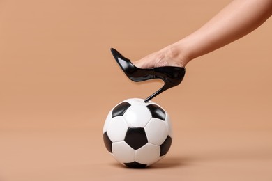 Photo of Woman in high heeled shoe with soccer ball on beige background, closeup