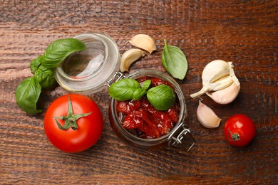 Photo of Delicious sun dried tomatoes in glass jar, fresh vegetables and spices on wooden table, flat lay