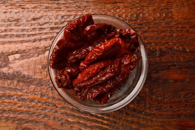 Photo of Delicious sun dried tomatoes in glass bowl on wooden table, top view