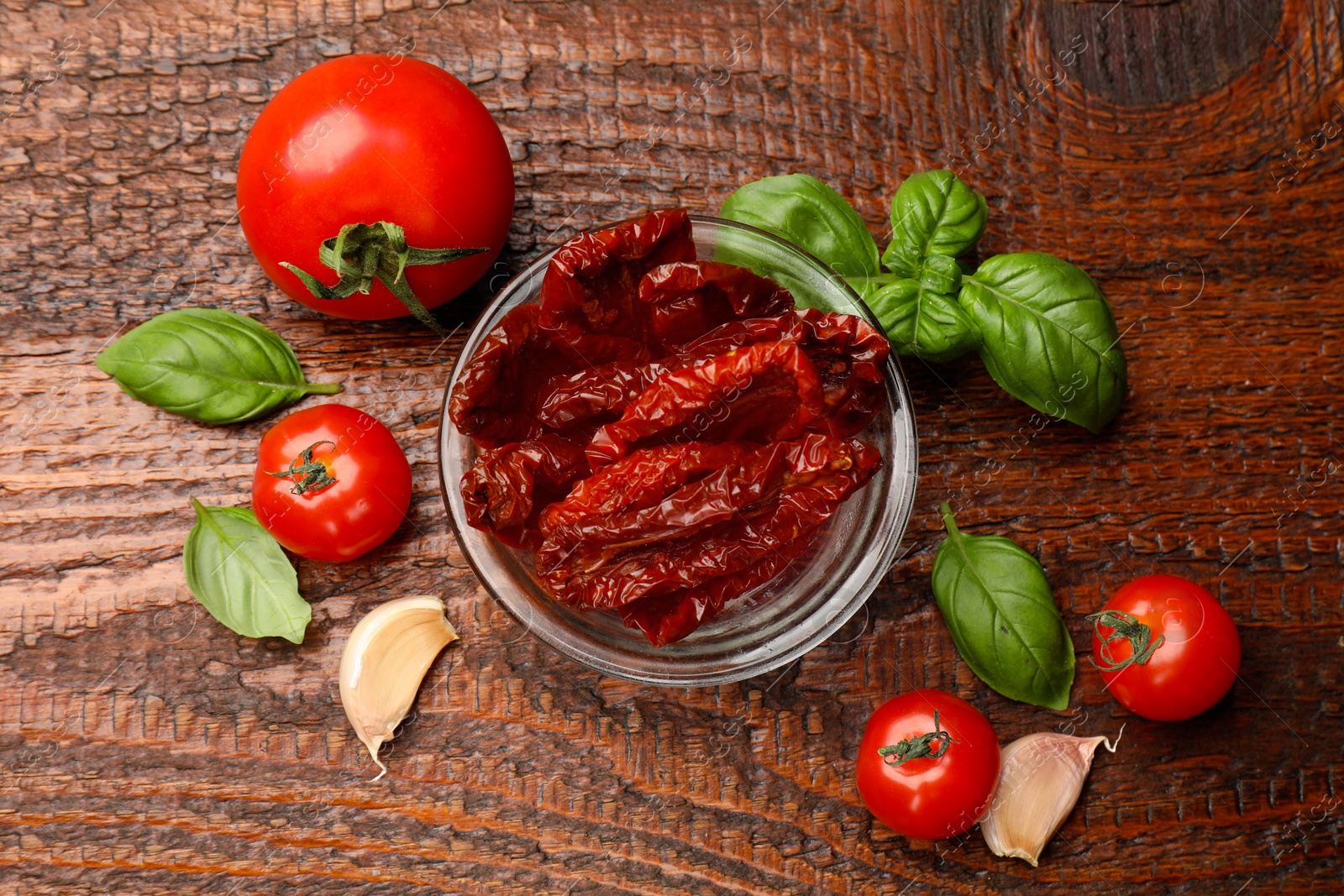 Delicious sun dried tomatoes in glass bowl, fresh vegetables and spices on wooden table, flat lay Photo of Delicious sun dried tomatoes in glass bowl, fresh vegetables and spices on wooden table, flat lay