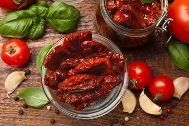 Photo of Delicious sun dried tomatoes in glass dishware, fresh vegetables and spices on wooden table, flat lay
