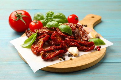 Photo of Delicious sun dried tomatoes, fresh vegetables and basil on light blue wooden table, closeup