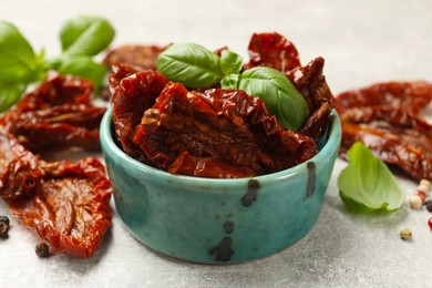 Photo of Delicious sun dried tomatoes in bowl and spices on gray textured table, closeup