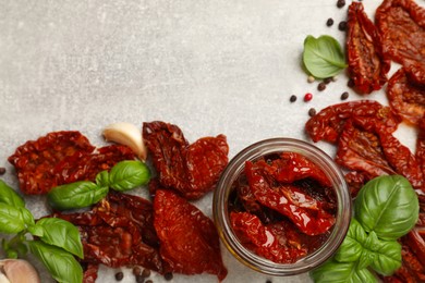 Photo of Delicious sun dried tomatoes in jar and spices on gray textured table, flat lay. Space for text