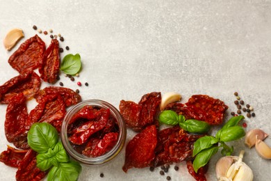 Photo of Delicious sun dried tomatoes in jar and spices on gray textured table, flat lay. Space for text