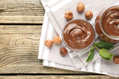 Photo of Tasty chocolate spread, hazelnuts and mint on wooden table, top view. Space for text