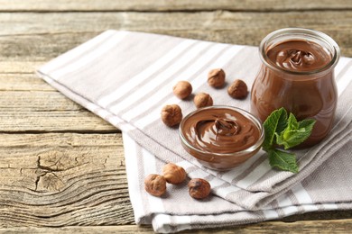 Photo of Tasty chocolate spread, hazelnuts and mint on wooden table, closeup
