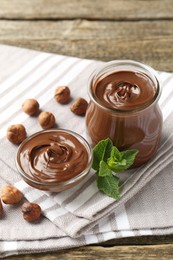 Photo of Tasty chocolate spread, hazelnuts and mint on wooden table