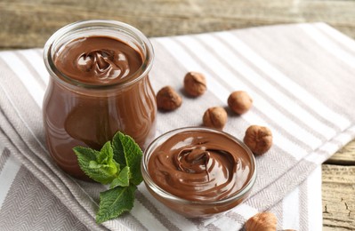 Photo of Tasty chocolate spread, hazelnuts and mint on wooden table, closeup