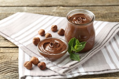 Photo of Tasty chocolate spread, hazelnuts and mint on wooden table, closeup