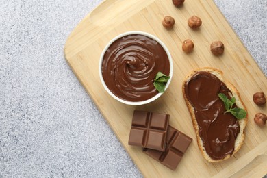 Photo of Tasty chocolate spread, toast, hazelnuts and mint on grey textured table, top view. Space for text