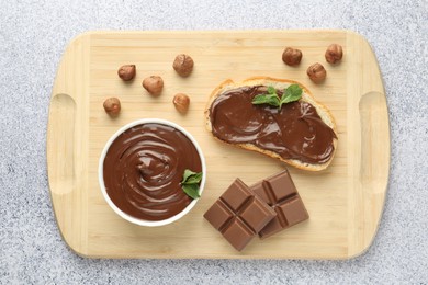Photo of Tasty chocolate spread, toast, hazelnuts and mint on grey textured table, top view