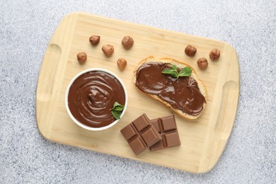 Photo of Tasty chocolate spread, toast, hazelnuts and mint on grey textured table, top view