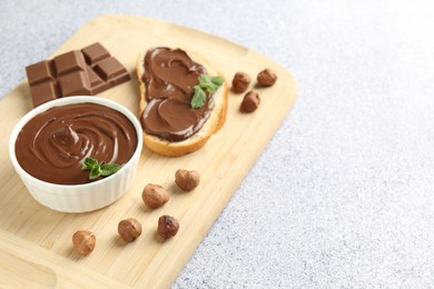 Photo of Tasty chocolate spread, toast, hazelnuts and mint on grey textured table, closeup. Space for text