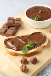 Photo of Tasty chocolate spread, toast, hazelnuts and mint on grey textured table, closeup