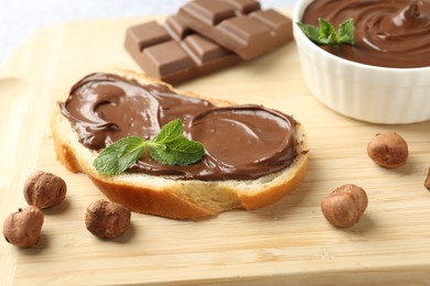 Photo of Tasty toast with chocolate spread, hazelnuts and mint on wooden board, closeup