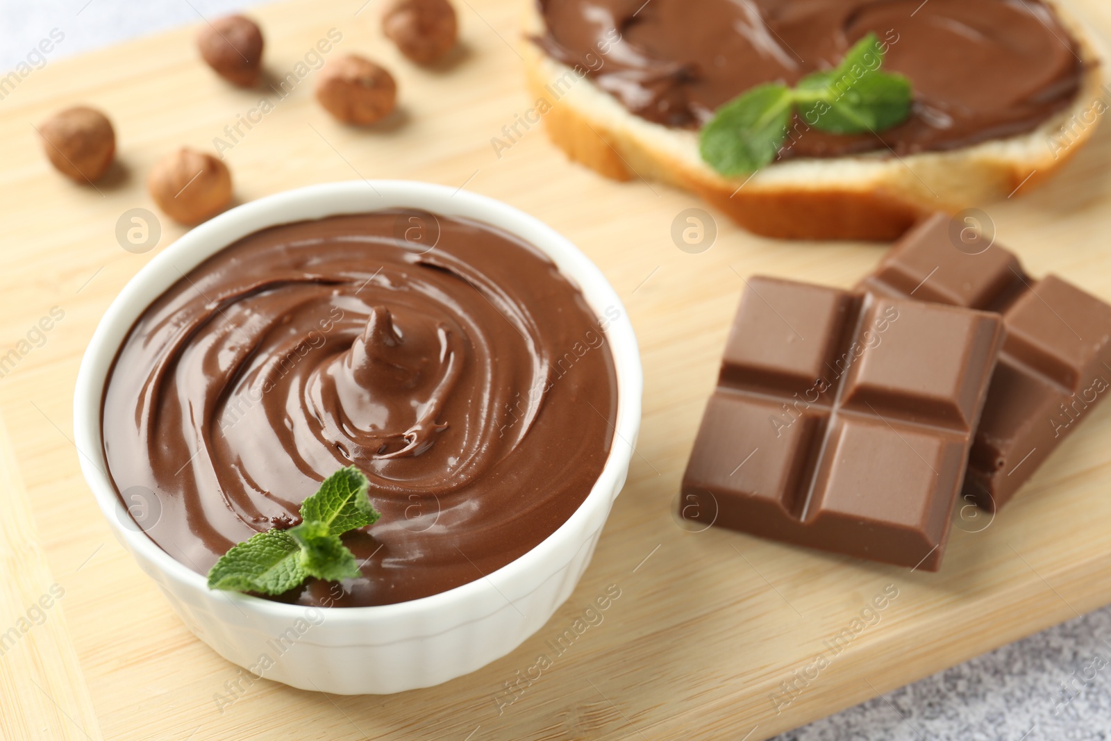 Photo of Tasty chocolate hazelnut spread with mint in bowl on table, closeup