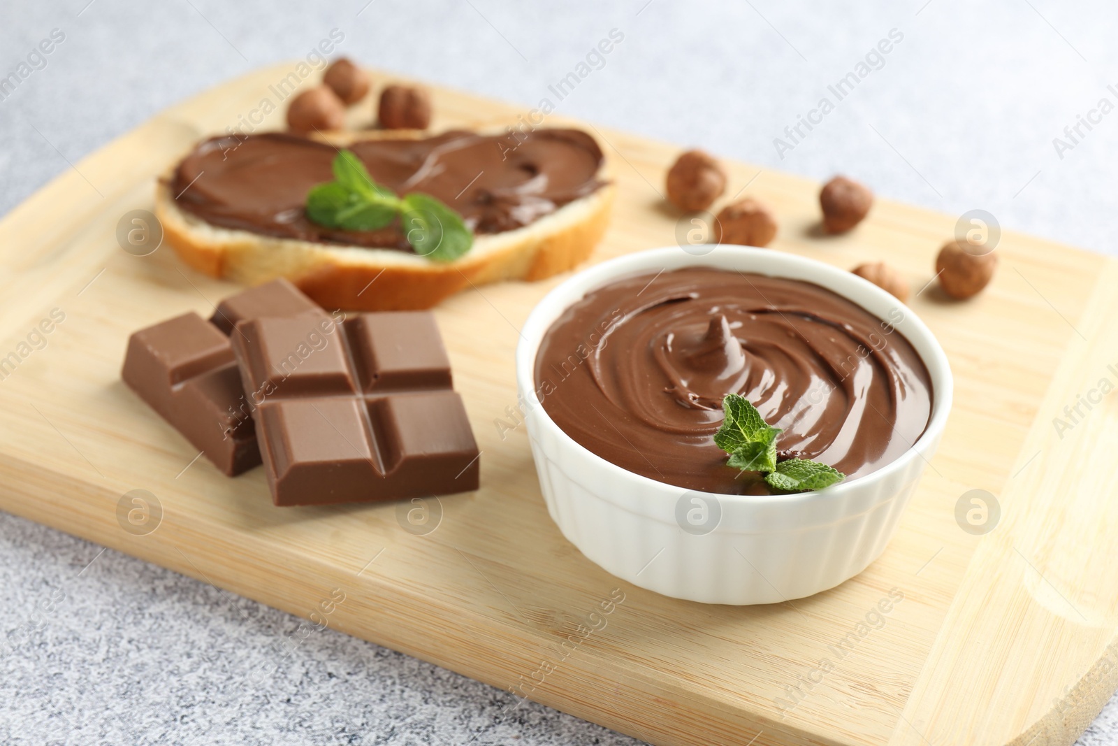 Photo of Tasty chocolate hazelnut spread with mint in bowl on grey textured table, closeup