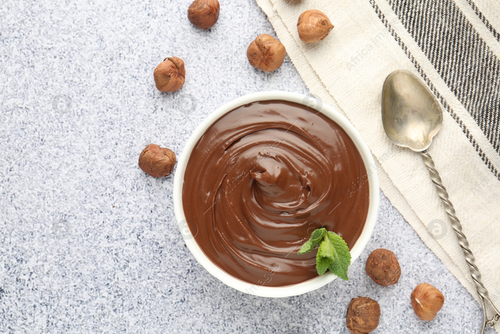 Tasty chocolate spread with mint in bowl and hazelnuts on grey textured table, flat lay Photo of Tasty chocolate spread with mint in bowl and hazelnuts on grey textured table, flat lay