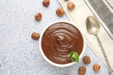 Photo of Tasty chocolate spread with mint in bowl and hazelnuts on grey textured table, flat lay
