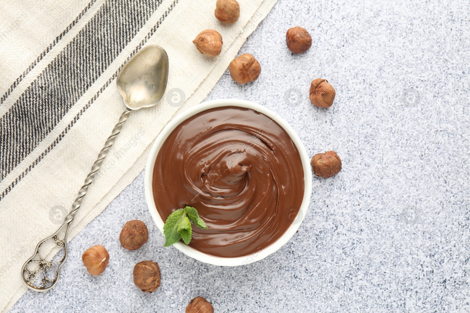 Tasty chocolate spread with mint in bowl and hazelnuts on grey textured table, flat lay Photo of Tasty chocolate spread with mint in bowl and hazelnuts on grey textured table, flat lay