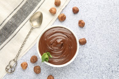 Tasty chocolate spread with mint in bowl and hazelnuts on grey textured table, flat lay