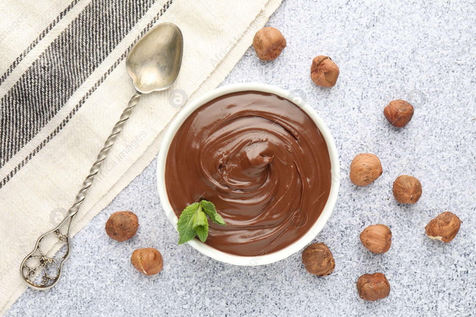Tasty chocolate spread with mint in bowl and hazelnuts on grey textured table, flat lay Photo of Tasty chocolate spread with mint in bowl and hazelnuts on grey textured table, flat lay