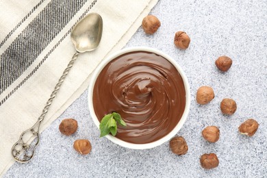 Photo of Tasty chocolate spread with mint in bowl and hazelnuts on grey textured table, flat lay