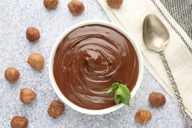 Photo of Tasty chocolate spread with mint in bowl and hazelnuts on grey textured table, flat lay