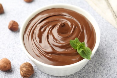 Photo of Tasty chocolate spread with mint in bowl and hazelnuts on grey textured table, closeup