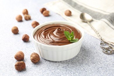 Photo of Tasty chocolate spread with mint in bowl and hazelnuts on grey textured table, closeup