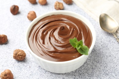 Photo of Tasty chocolate spread with mint in bowl and hazelnuts on grey textured table, closeup