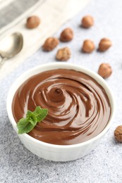 Photo of Tasty chocolate spread with mint in bowl and hazelnuts on grey textured table