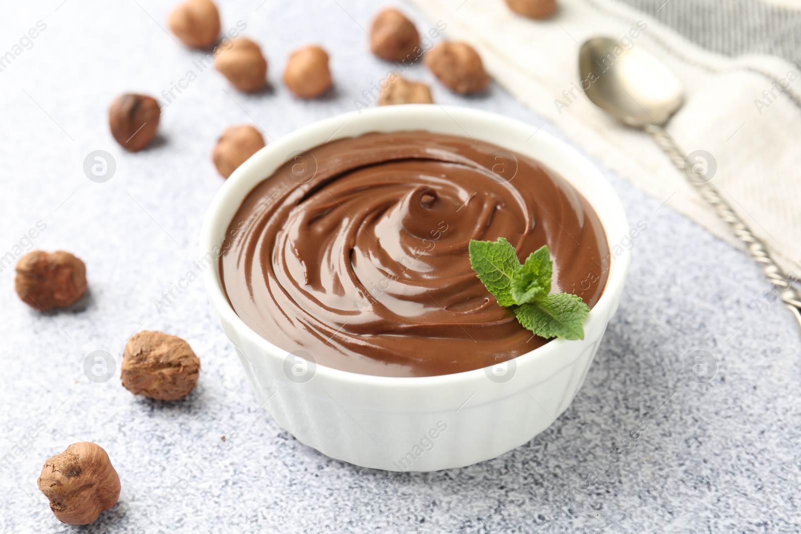 Tasty chocolate spread with mint in bowl and hazelnuts on grey textured table, closeup Photo of Tasty chocolate spread with mint in bowl and hazelnuts on grey textured table, closeup