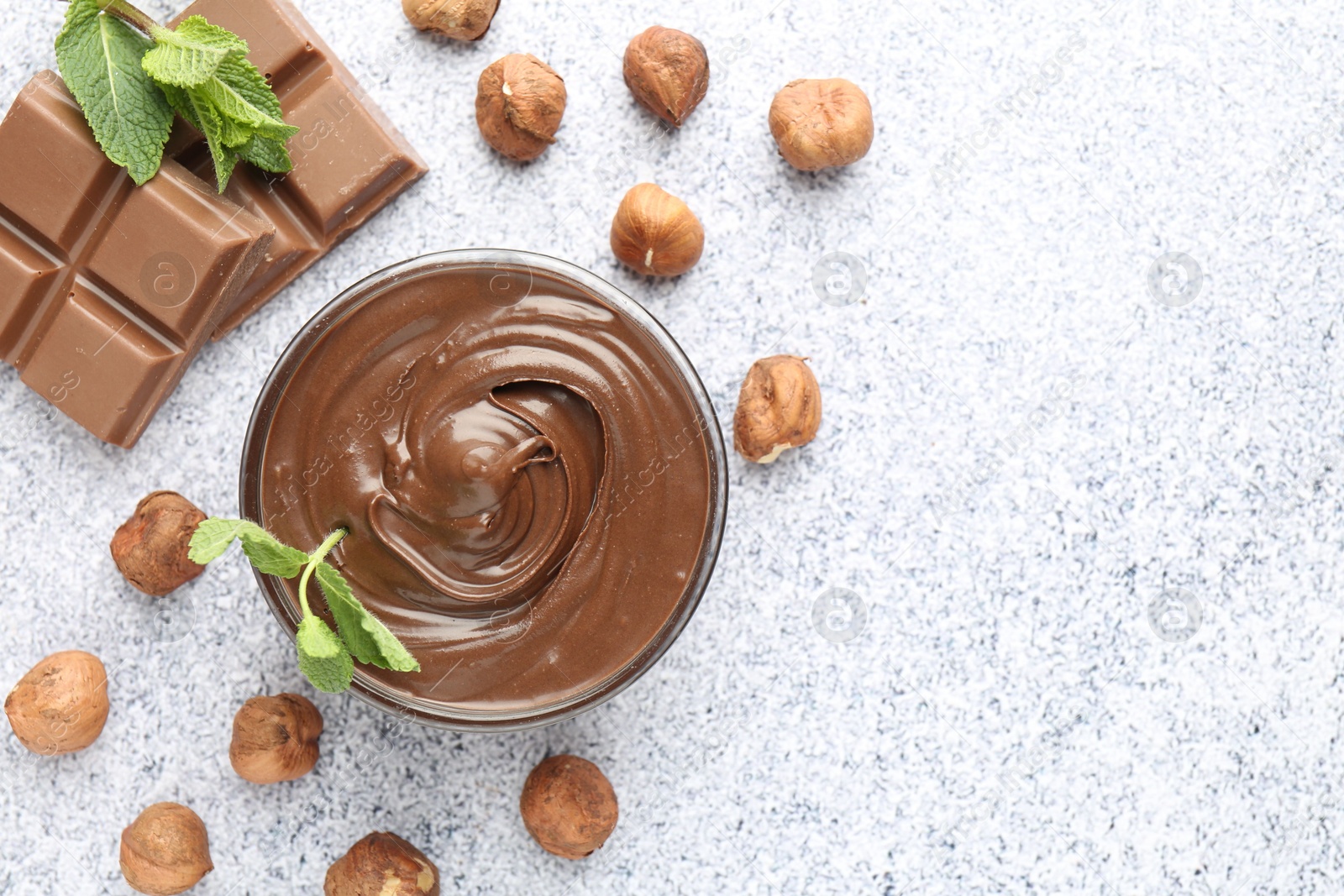 Tasty chocolate spread with mint in bowl and hazelnuts on grey textured table, flat lay. Space for text Photo of Tasty chocolate spread with mint in bowl and hazelnuts on grey textured table, flat lay. Space for text