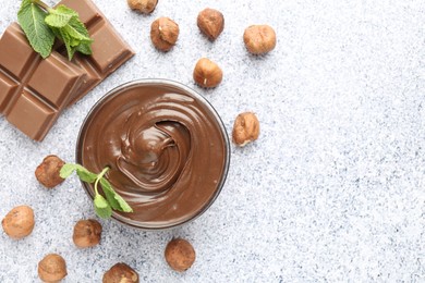 Photo of Tasty chocolate spread with mint in bowl and hazelnuts on grey textured table, flat lay. Space for text