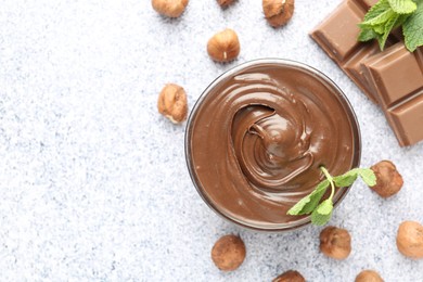 Photo of Tasty chocolate spread with mint in bowl and hazelnuts on grey textured table, flat lay. Space for text