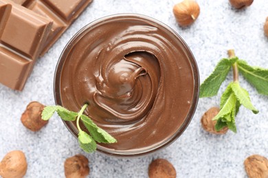 Photo of Tasty chocolate spread with mint in bowl and hazelnuts on grey textured table, flat lay