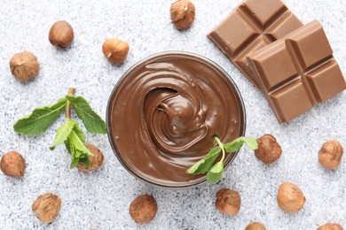 Photo of Tasty chocolate spread with mint in bowl and hazelnuts on grey textured table, flat lay