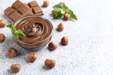 Photo of Tasty chocolate spread with mint in bowl and hazelnuts on grey textured table, closeup. Space for text